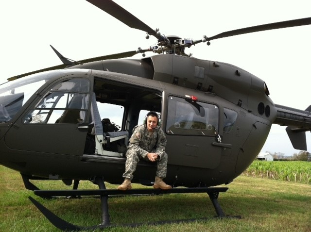 一名身着军装的男子坐在地面上直升飞机敞开的舱门内